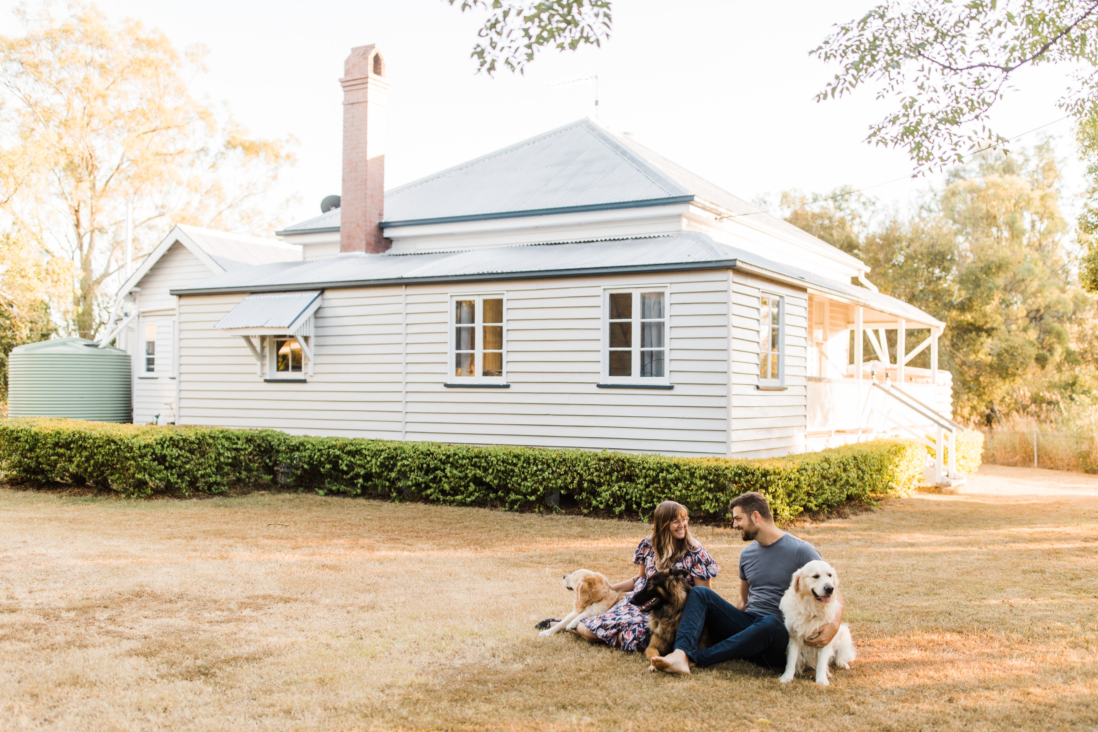 A couple and two dogs are sitting on the grass in front of a home discussing property finance.