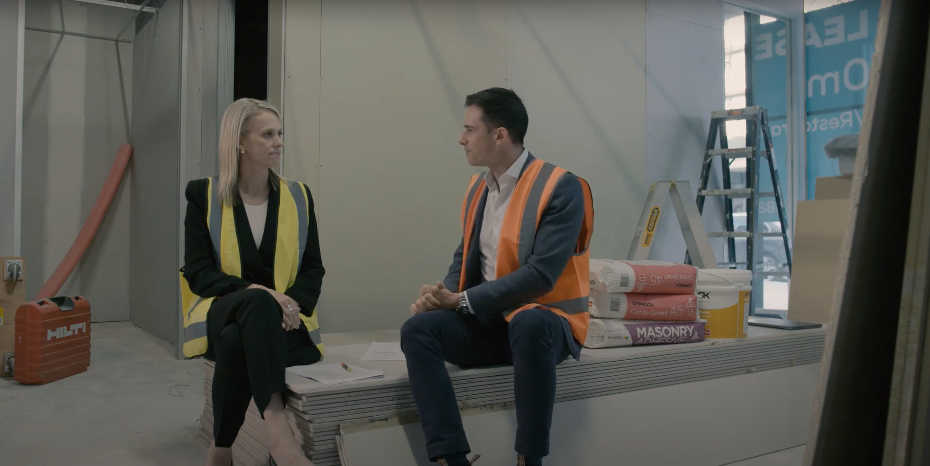 Dr Bronwyn King and Julian Muldoon, expert medical property consultant, sitting in a building undergoing a fit-out wearing high visibility vests.