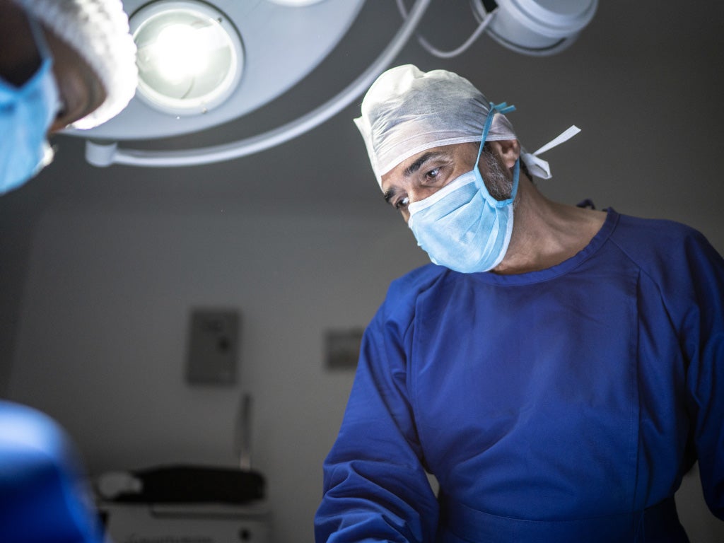 Surgeon in surgical mask, surgical cap looking over patient on operating table