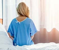 Patient sitting on edge of hospital bed in gown
