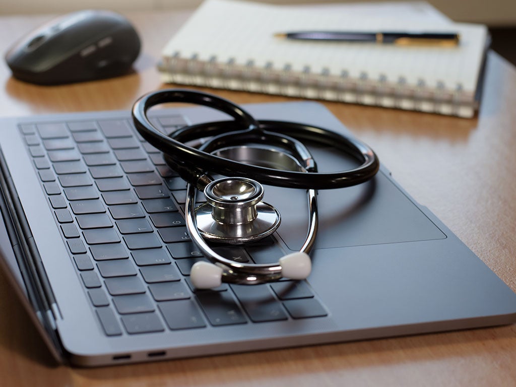 Black stethoscope sitting on the keyboard of an apple laptop