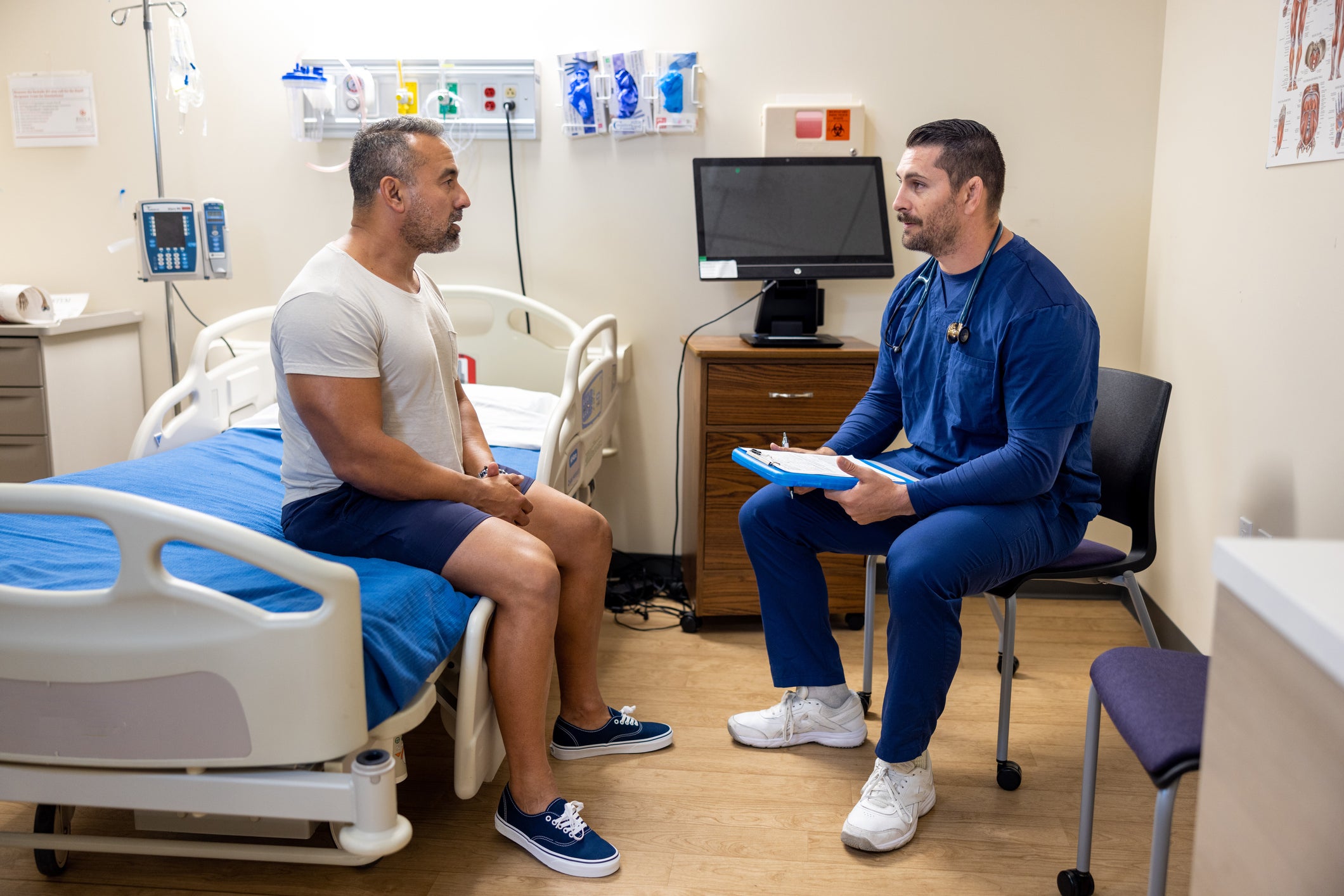 Doctor seeing patient who is sitting on hospital bed 