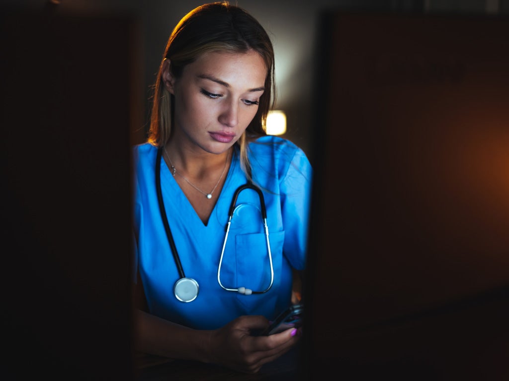 Young female in scrubs with stethoscope around her neck looking down