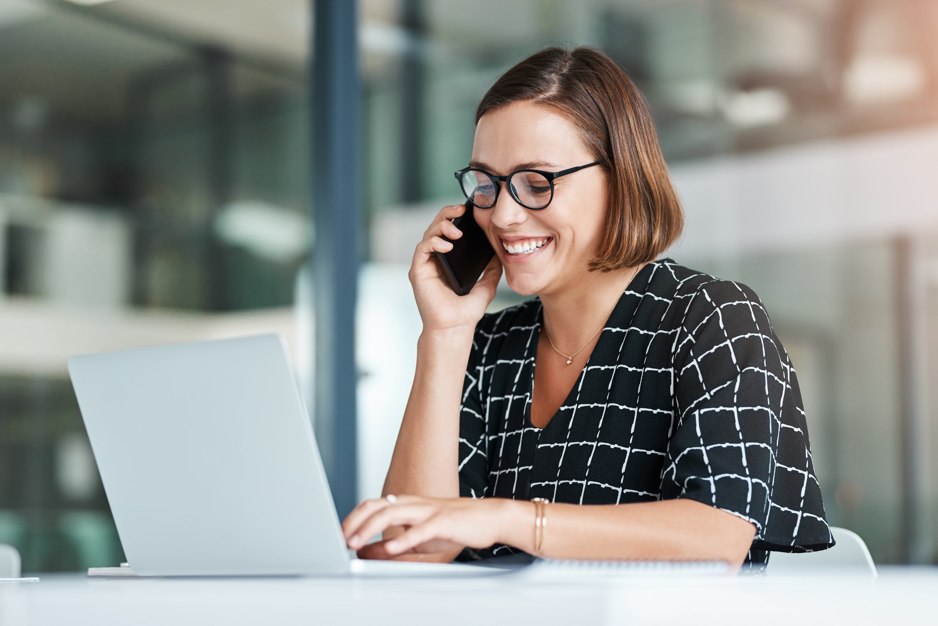 person on the phone smiling while working on their laptop