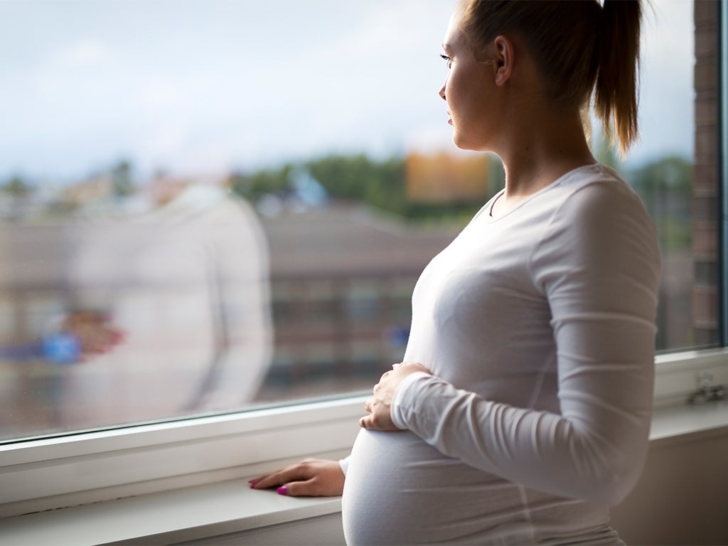 Pregnant woman looking out the window of apartment