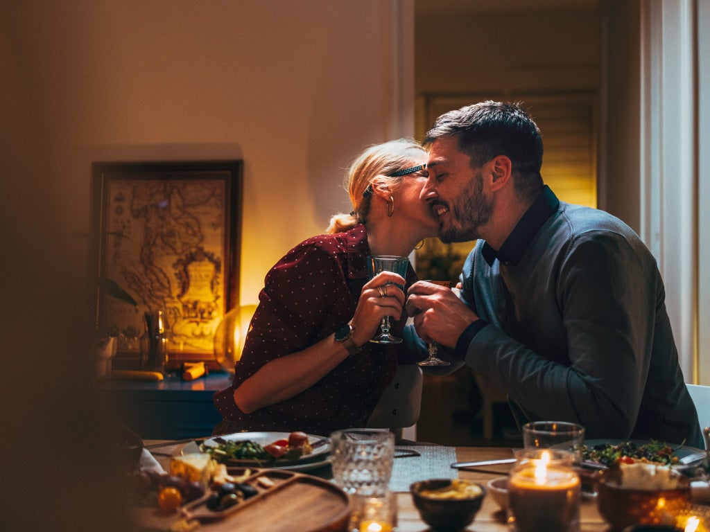 Woman and man having intimate dinner with wine kissing on cheek