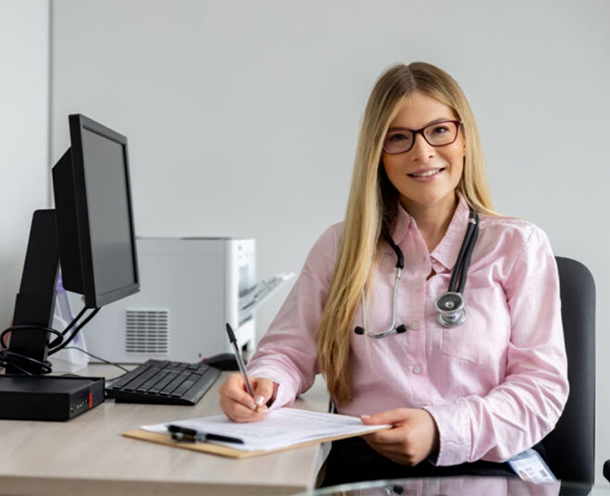 doctor sitting at desk writing on a clipboard