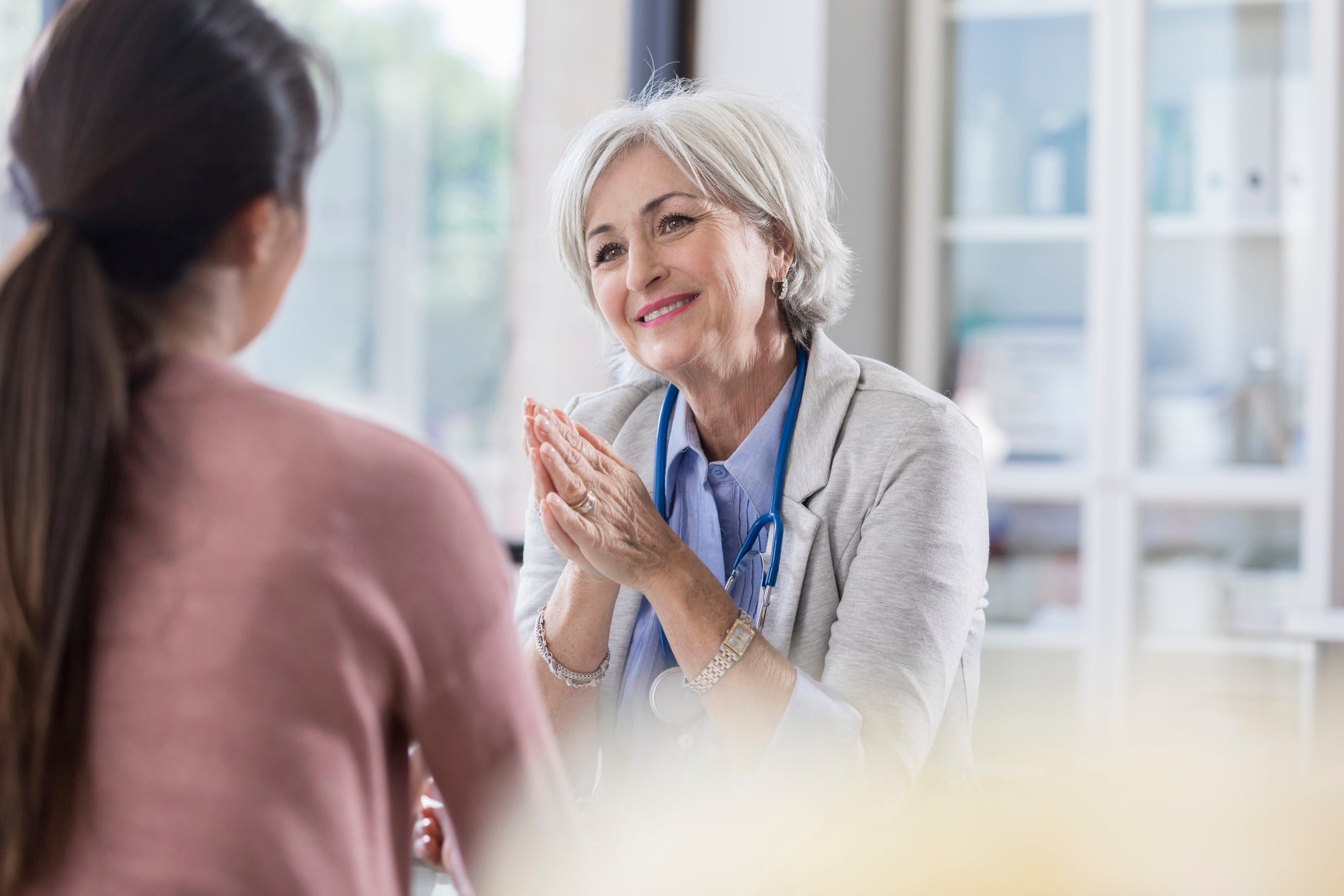 older female doctor smiling and talking to a young female patient 