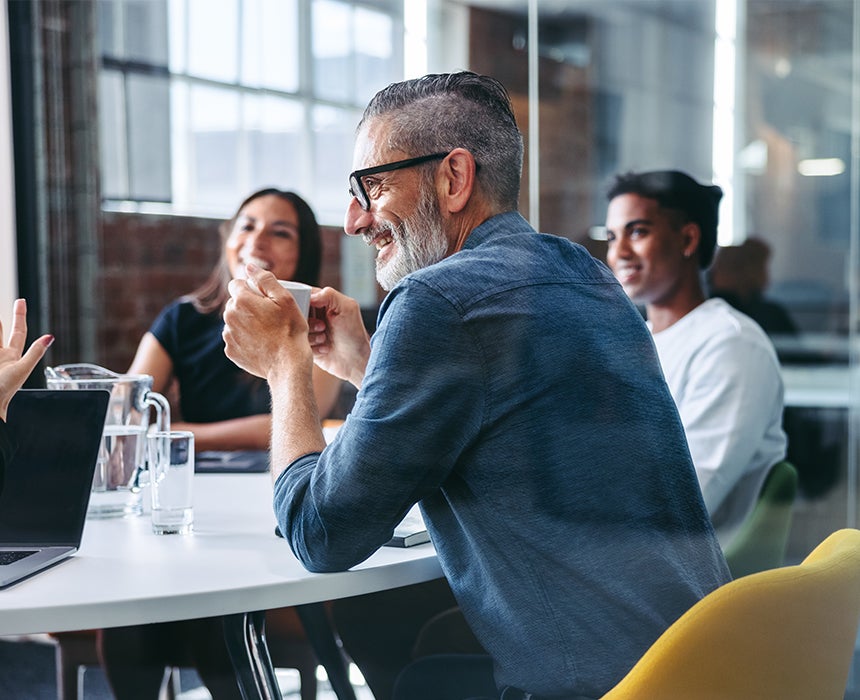 Photo of colleagues sitting around a table looking happy and engaged in discussion.