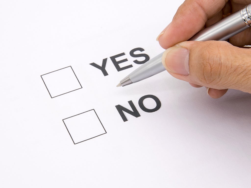 Hand holding pen which is hovering over two tick boxes, one with Yes and one with No