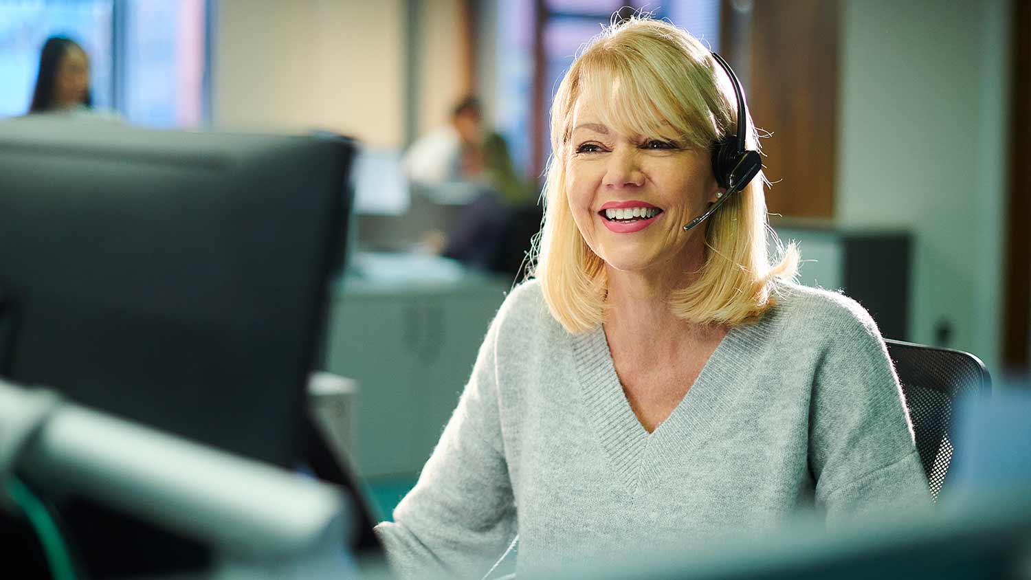 person wearing a headset talking and smiling in front of their computer