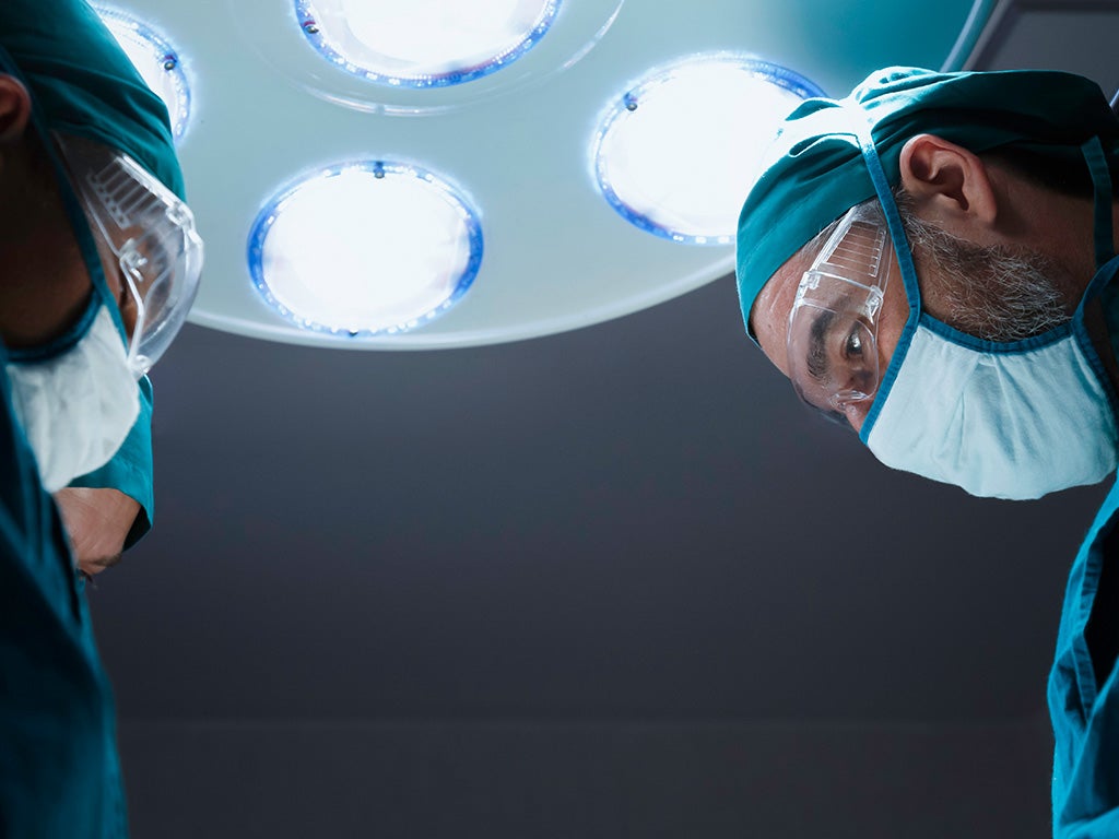 Two surgeons with surgical masks and safety glasses looking down onto operating table