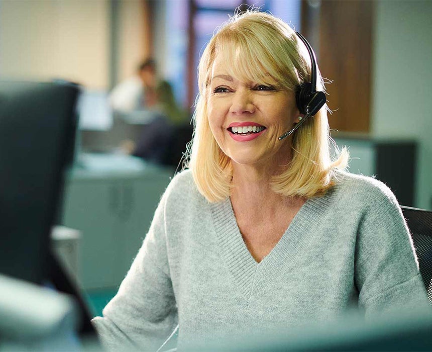 person wearing a headset talking and smiling in front of their computer