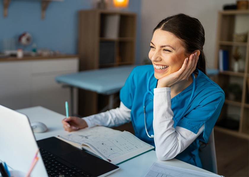 Nurse smiling at laptop while writing