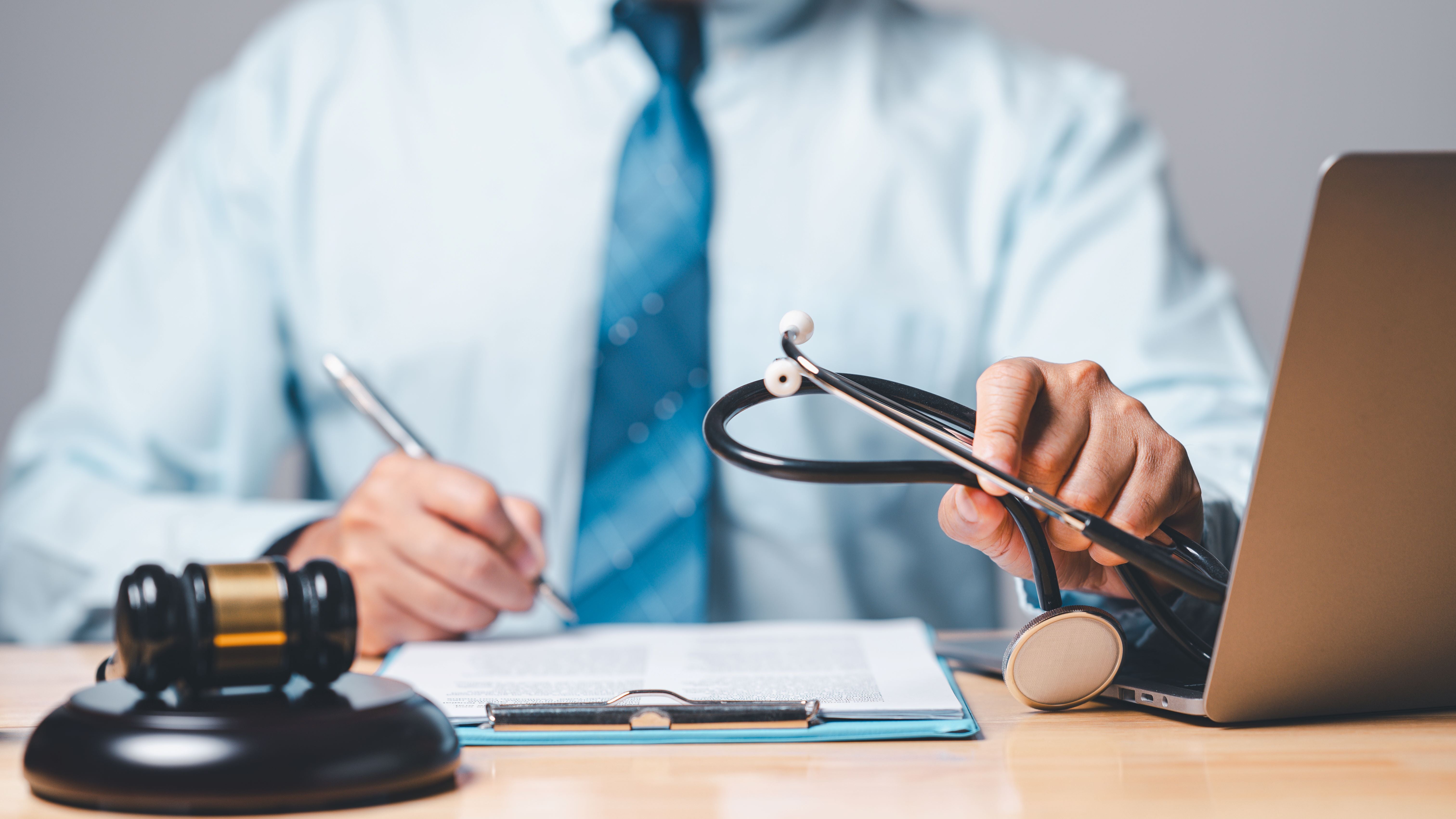 Doctor sitting writing report with gavel and stethoscope