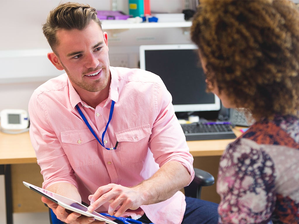 Male doctor in pink shirt talks to female patient