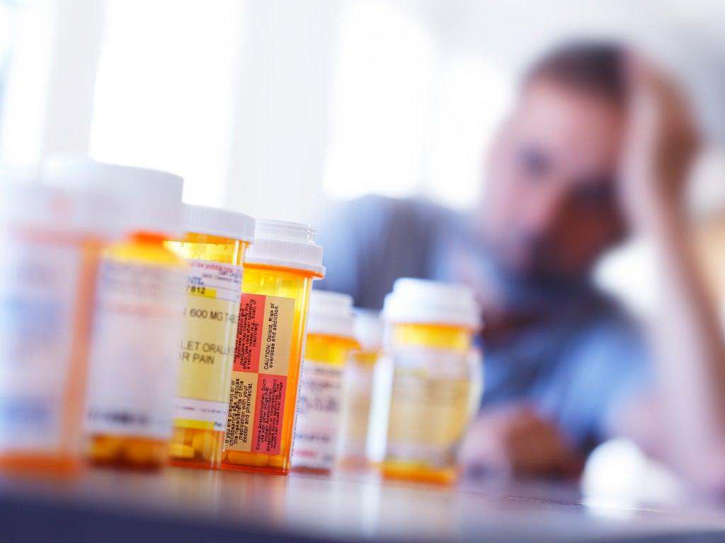 Medication bottle lined up in a row with male holding head in hand while sitting at table