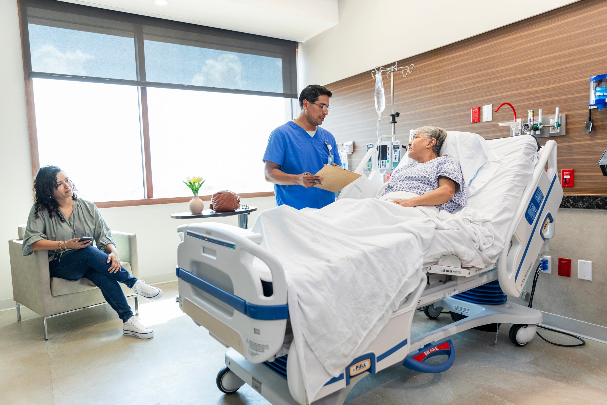 Surgeon standing next to patient bedside with medical file 