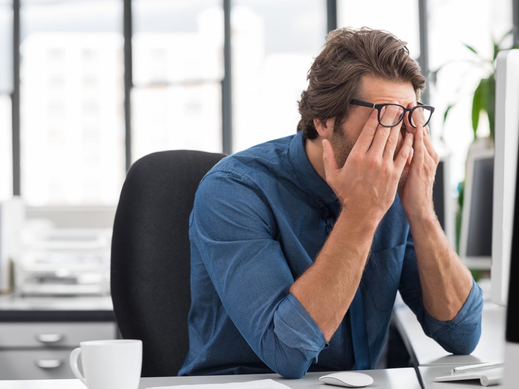 man rubbing eyes sitting at desk