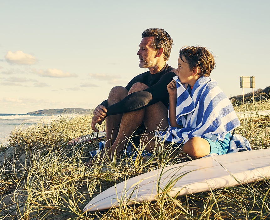 Father and son sitting on grass near beach