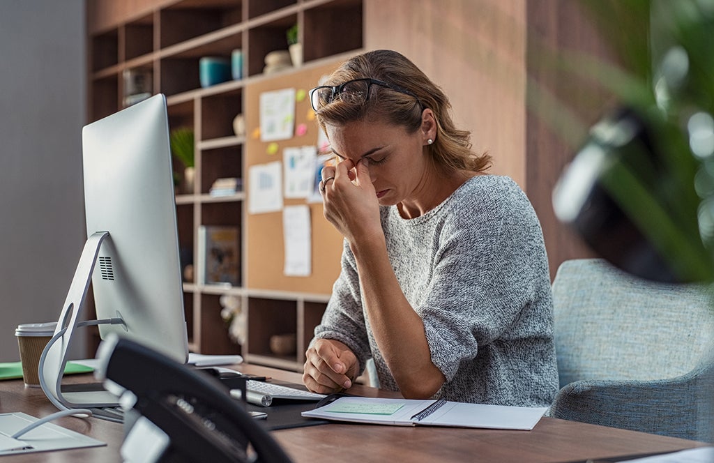 Woman stressed with hands on face at desk
