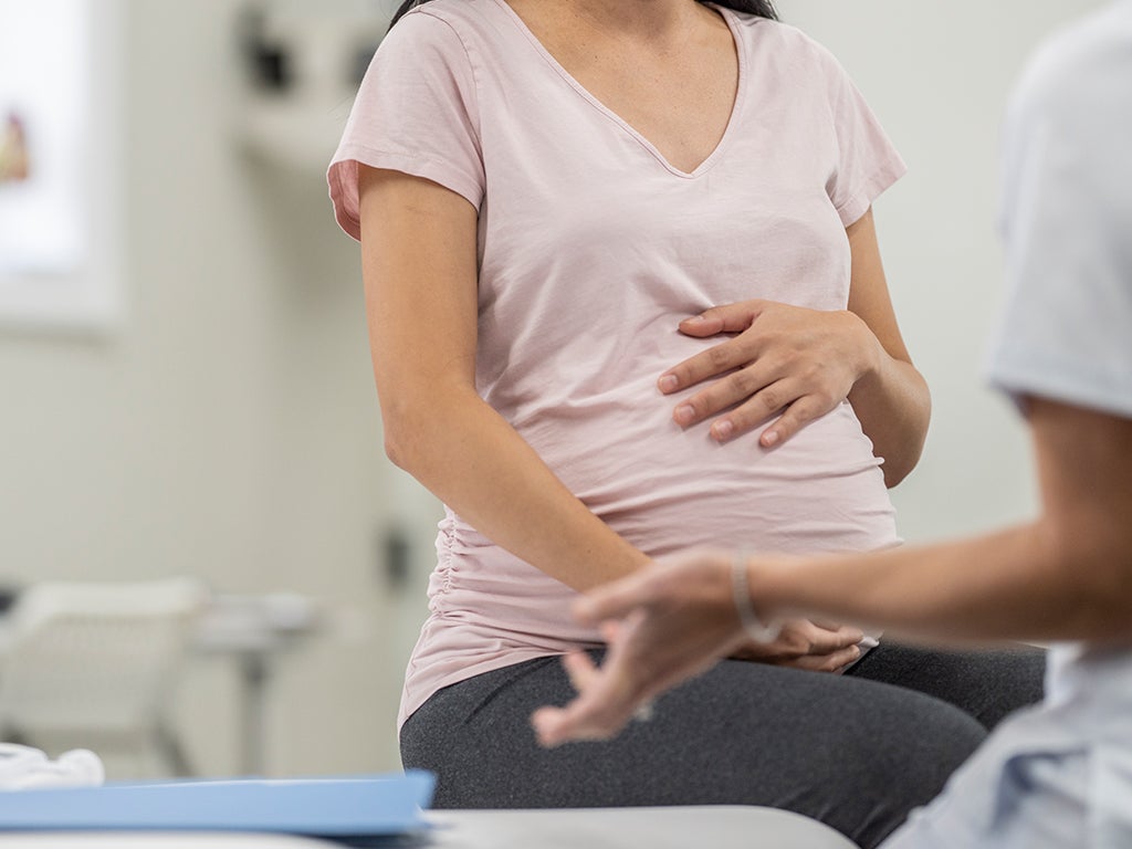 Pregnant woman sitting on examination table with hand rested on the top of her stomach