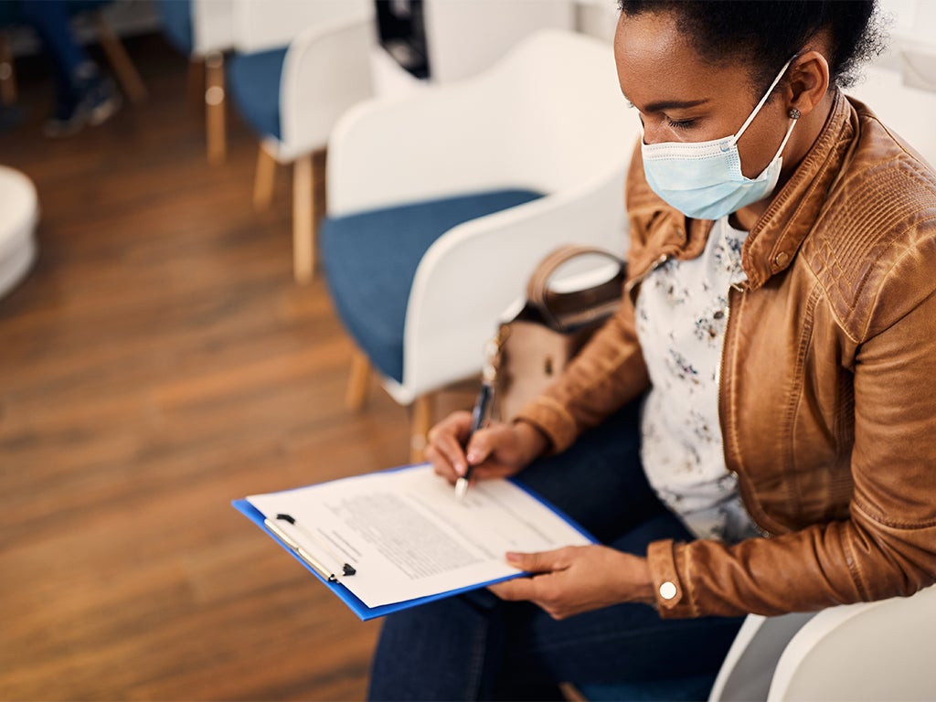 Patient sitting in waiting room with surgical mask on writing on a clip board