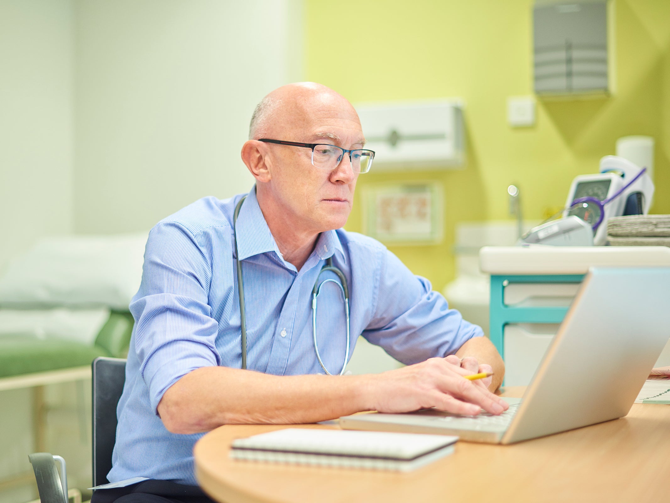 Older bald male GP typing on computer