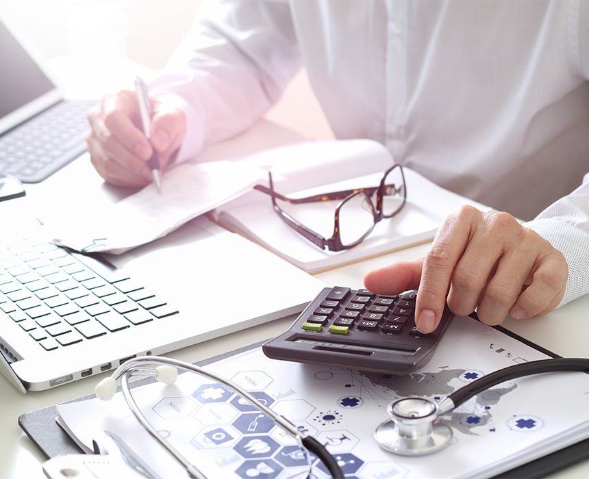 Doctor sitting at desk with calculator 