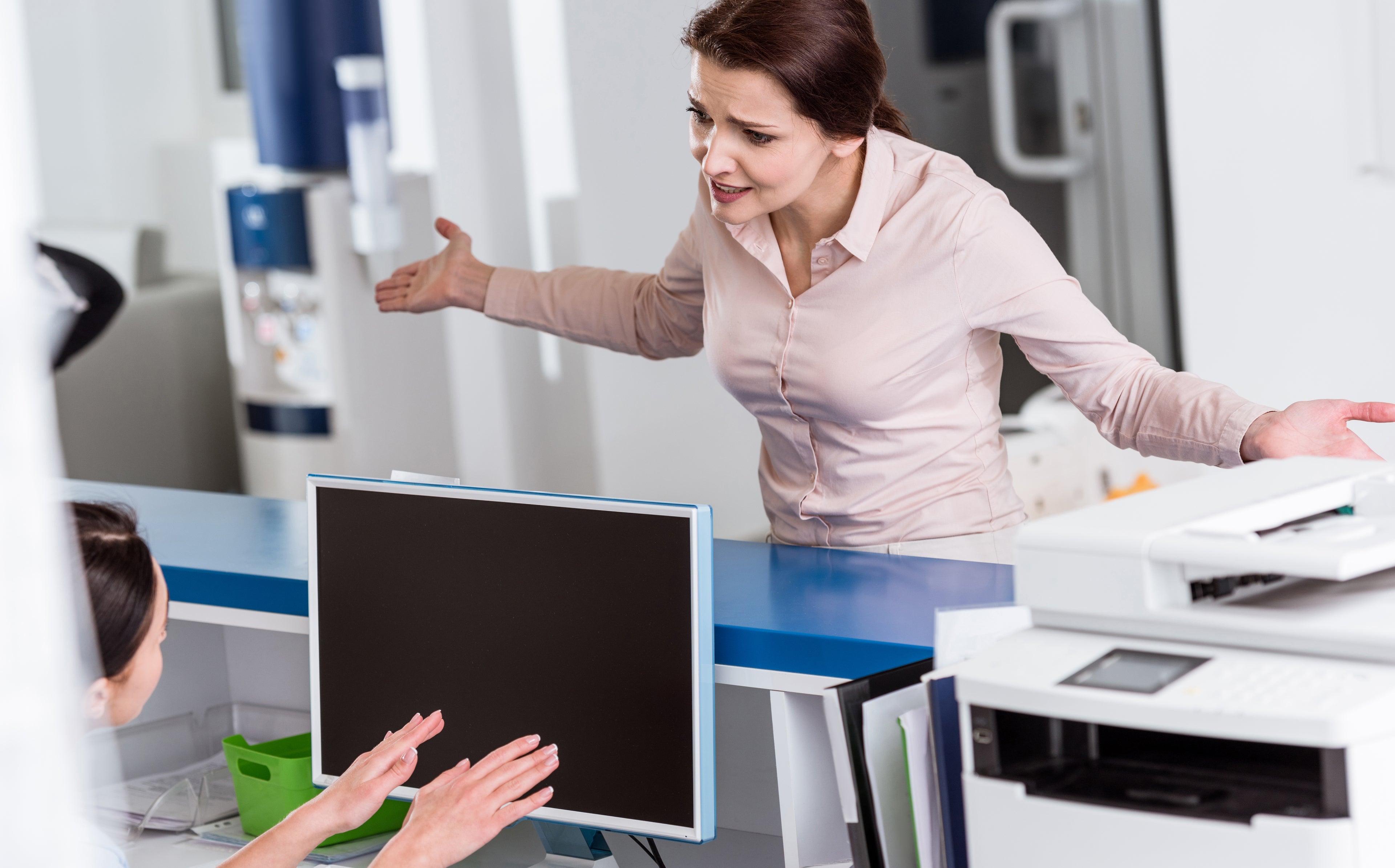 Person at front desk of medical practice with arms outstretched in frustration