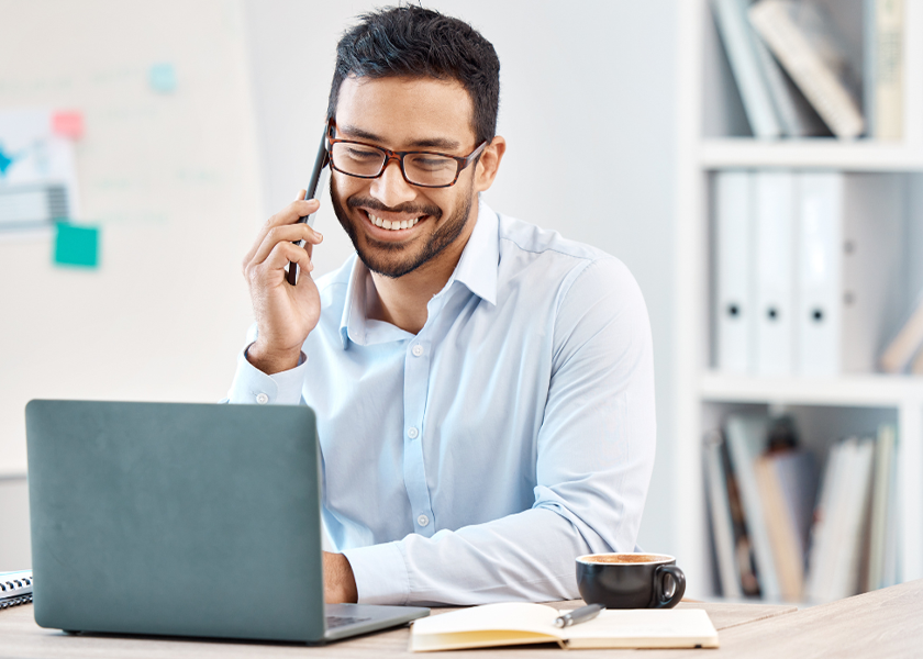 male smiling while on phone and using laptop