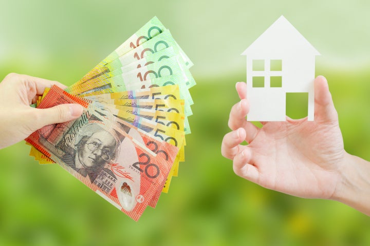 Hand holding money with the other hand holding a model house