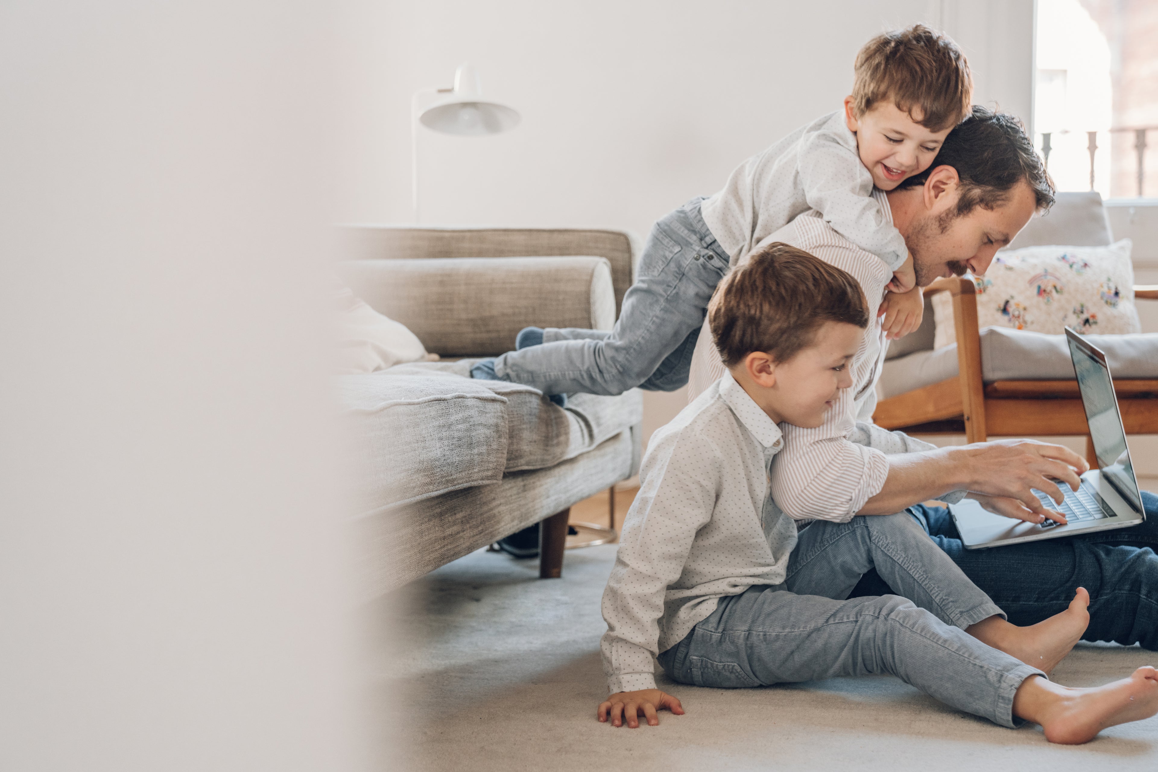 Two sons cuddling their father while he researches home loans for veterinary professionals on his laptop.