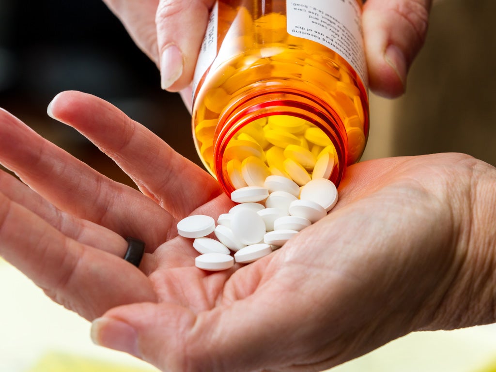 Person's hands tipping an orange pill bottle with white pills into open palm. 