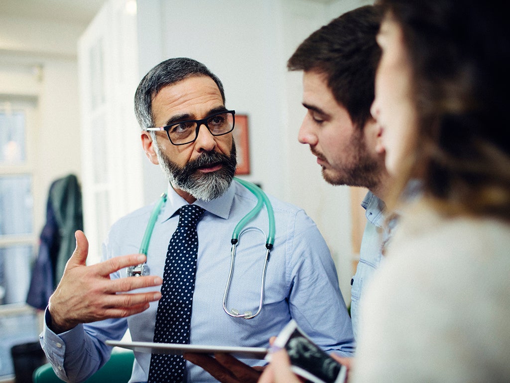 Older male doctor speaking to two patients