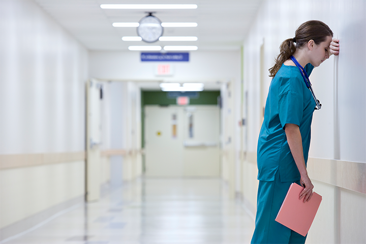 Junior medical professional with head on arm against a wall