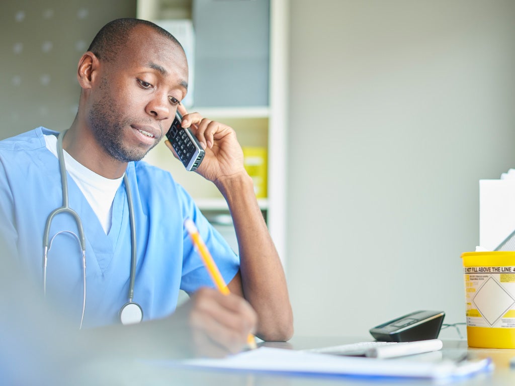 Doctor in scrubs holding a phone to his ear with his left hand looking down at paper