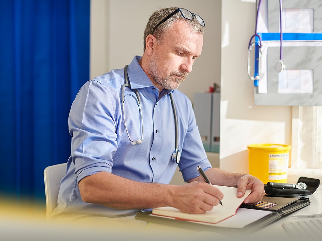 GP sitting next to hospital bed writing up consultation notes