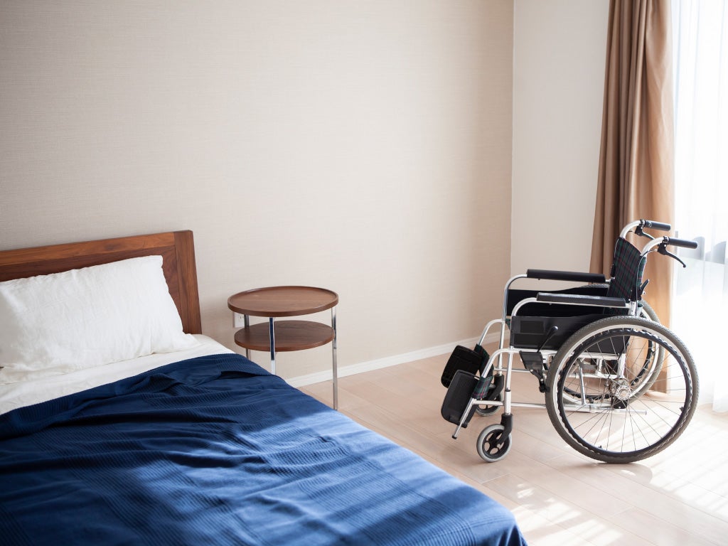 Bed room showing half of a double bed with a empty wheel chair between the bed and the window