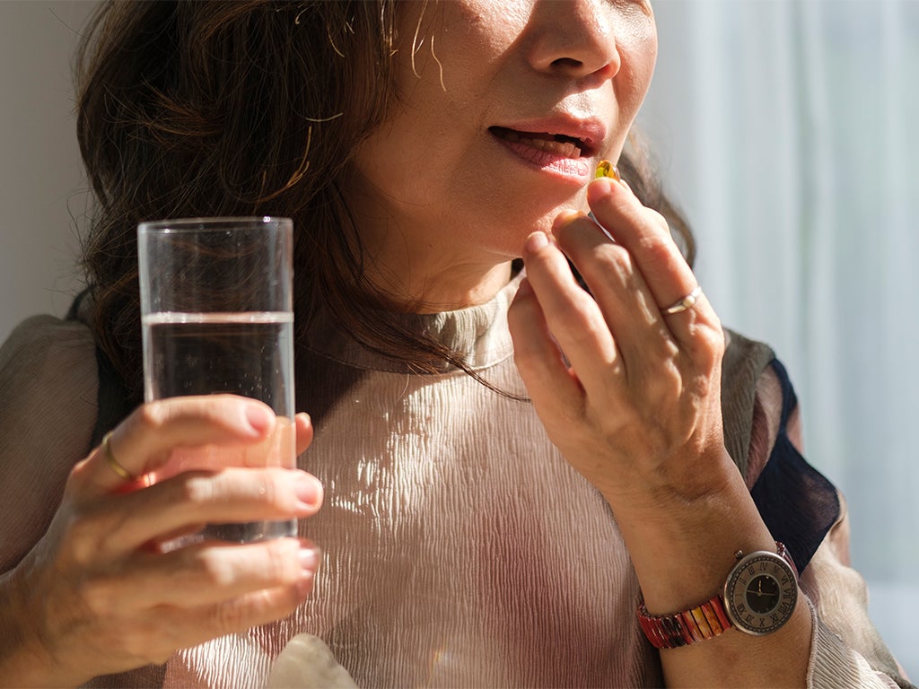 Middle aged woman taking pill with glass of water in her hand