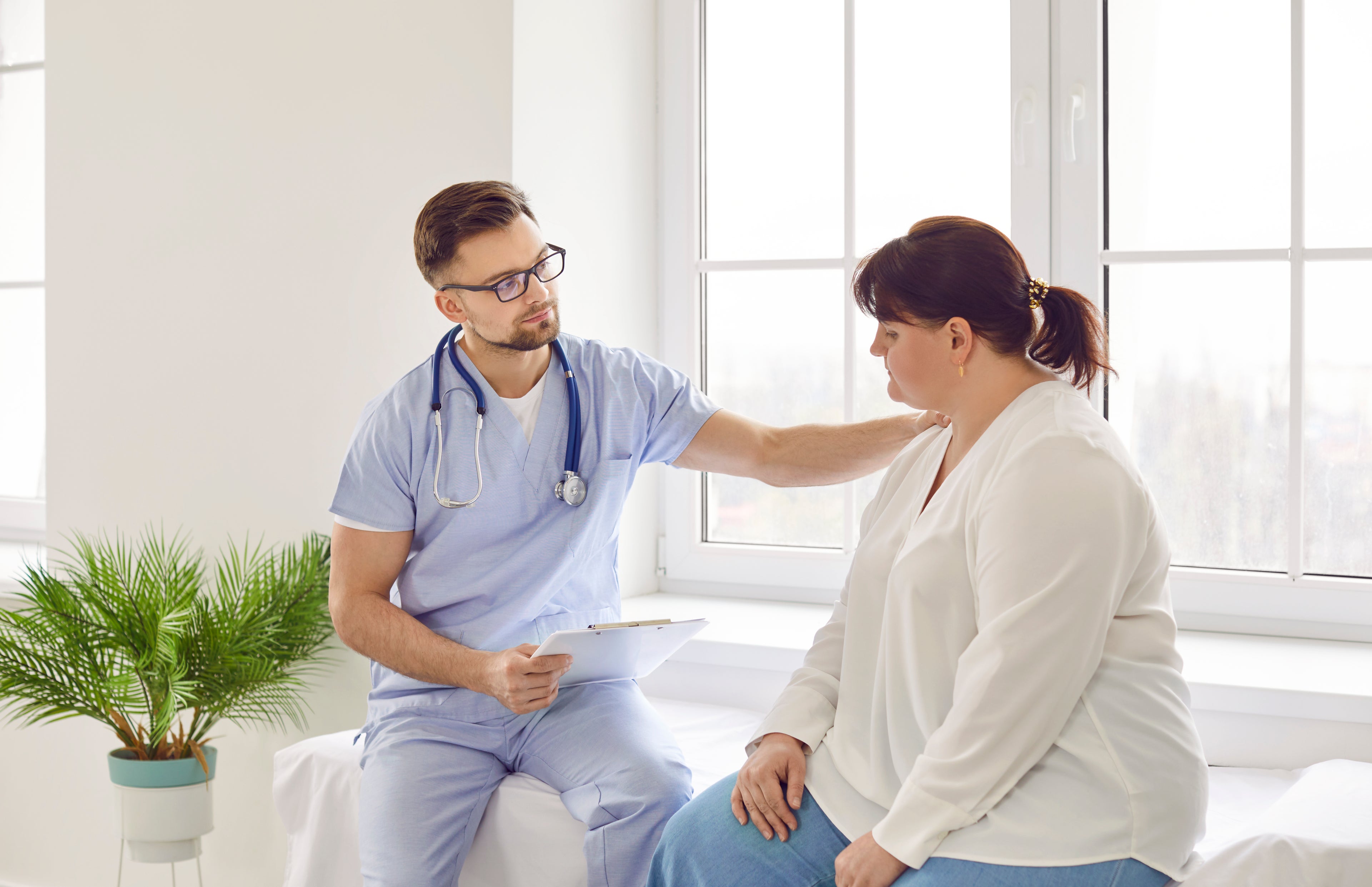 Doctor in scrubs sitting beside patient in hospital bed 