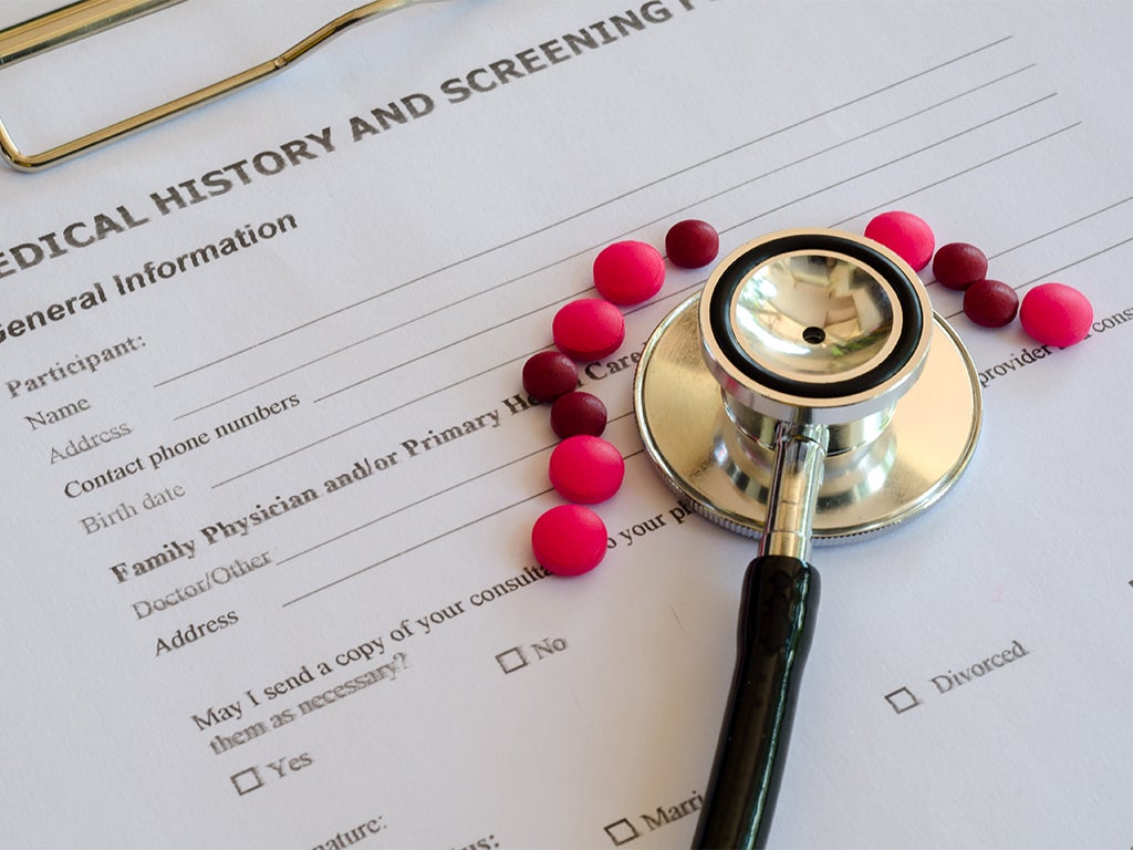 The bell end of a stethoscope resting on a medical information clipboard surrounded by pink medicine tablets