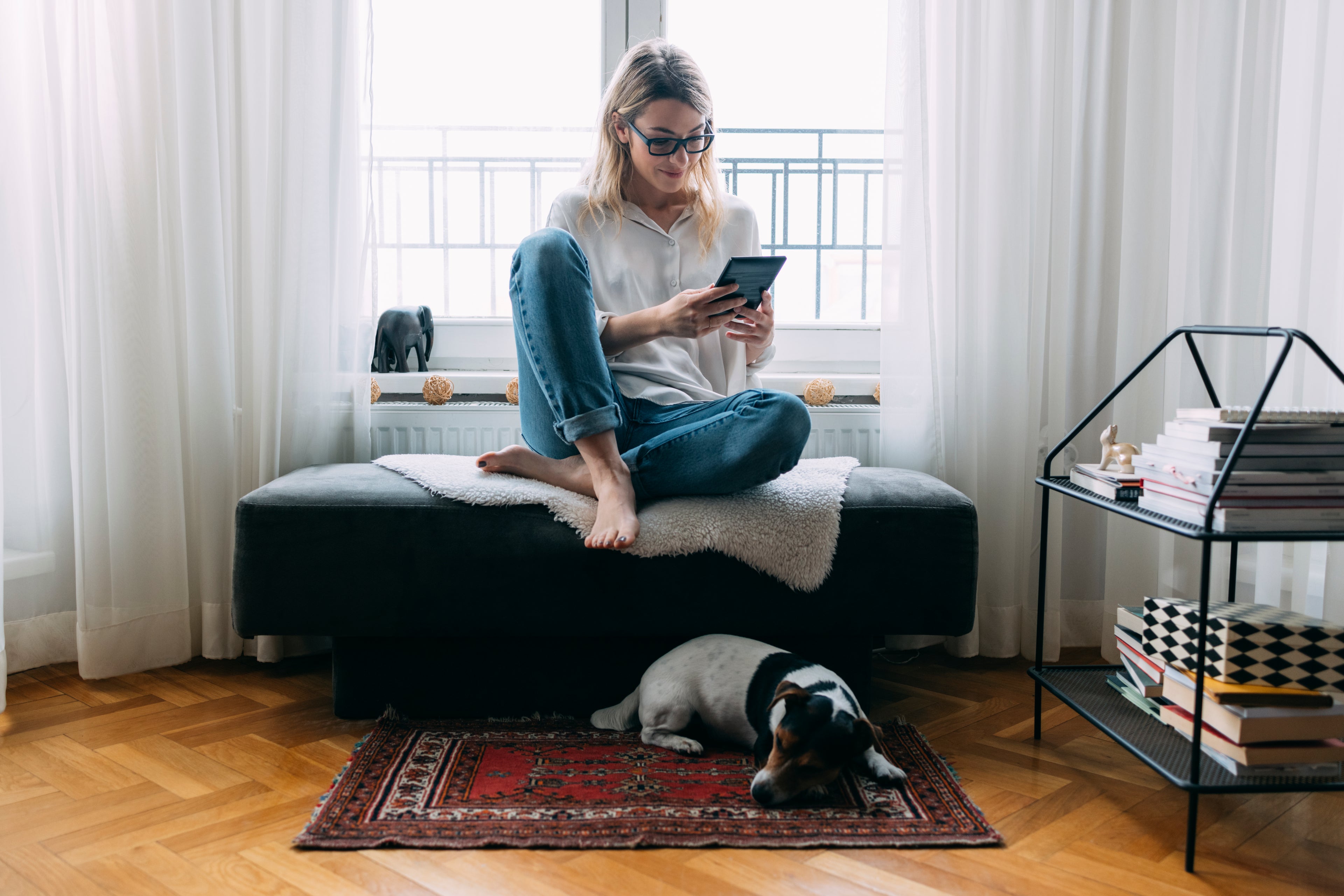 Woman sitting on an ottoman looking at an iPad. 