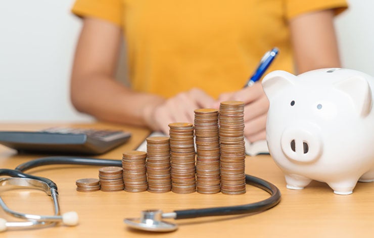 person sitting behind piggy bank, coins and stethoscope