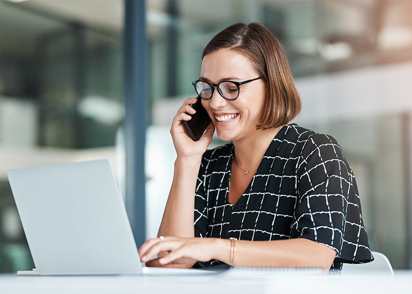 person on the phone smiling while working on their laptop