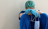 Doctor in scrubs sitting against a wall with head hung