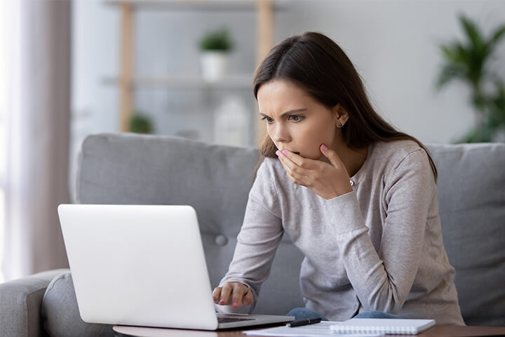 Woman stares at laptop with shocked expression